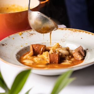 Fabada tradicional asturiana con fabes, chorizo y morcilla servida en plato hondo, terminándose de servir desde una olla.