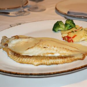 Filete de rodaballo servido con salsa Meunière en plato blanco, acompañado de guarnición de patata y brócoli.