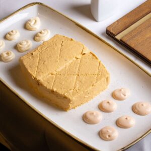 Pastel de cabracho casero servido en bloque rectangular con pequeños puntos de salsa, presentado en bandeja blanca.