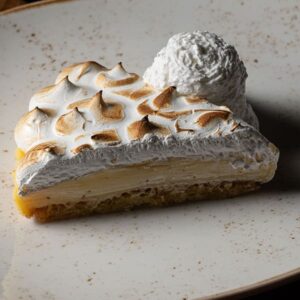 Porción de tarta de limón con merengue tostado y base crujiente, servida en plato beige.